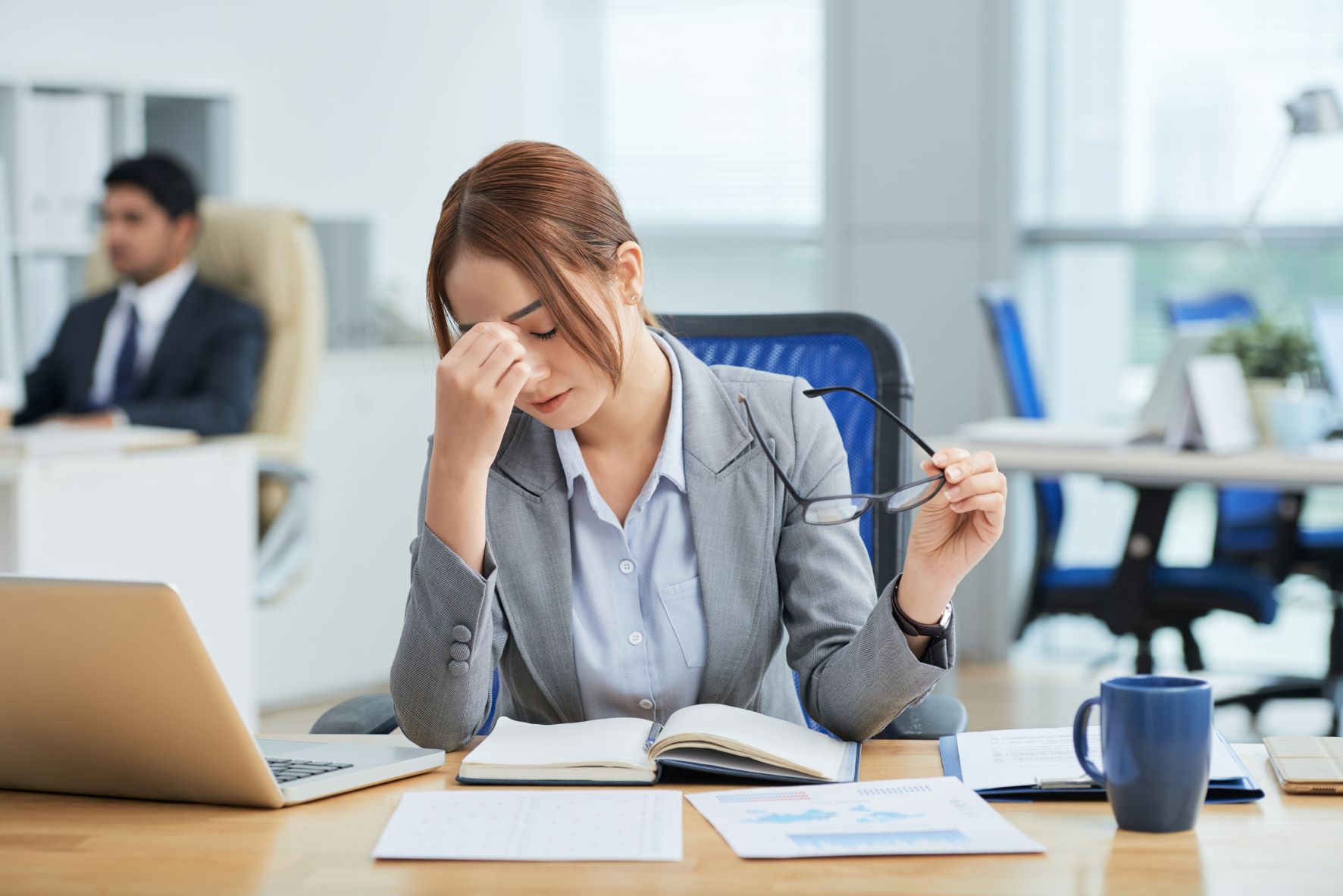 medium-shot-young-asian-woman-sitting-desk-office-rubbing-nose