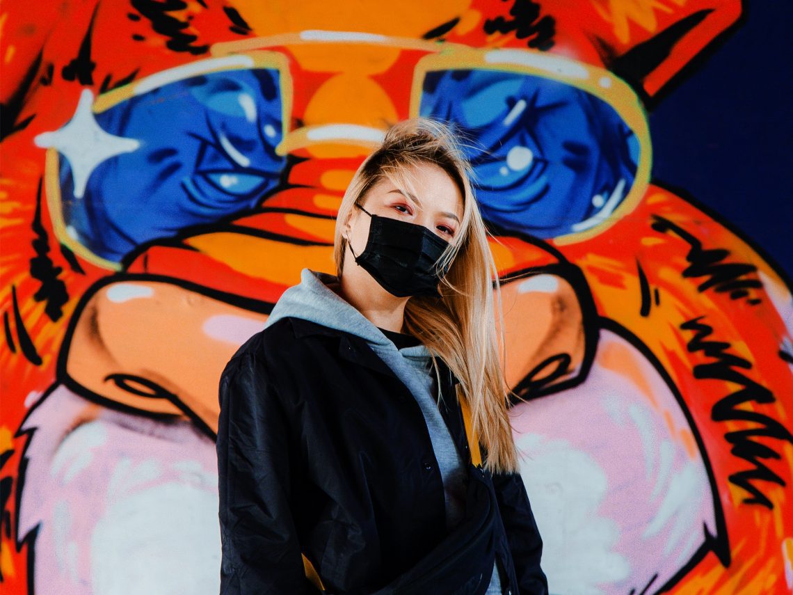 woman-in-black-jacket-wearing-a-mask-standing-beside-wall-3937901-1140x855