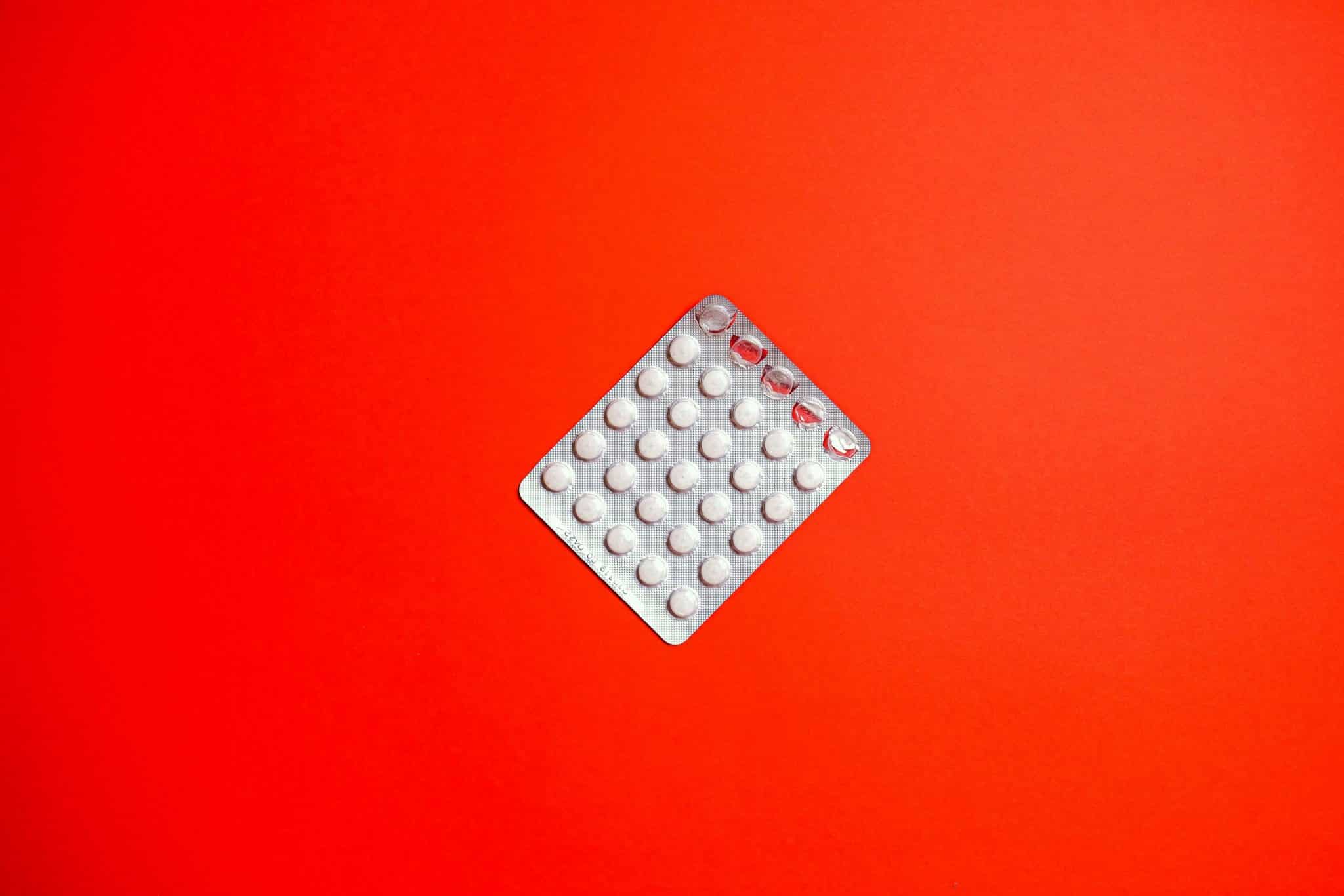 Close-up of a blister pack of pills against a solid red background symbolizing healthcare and medication.