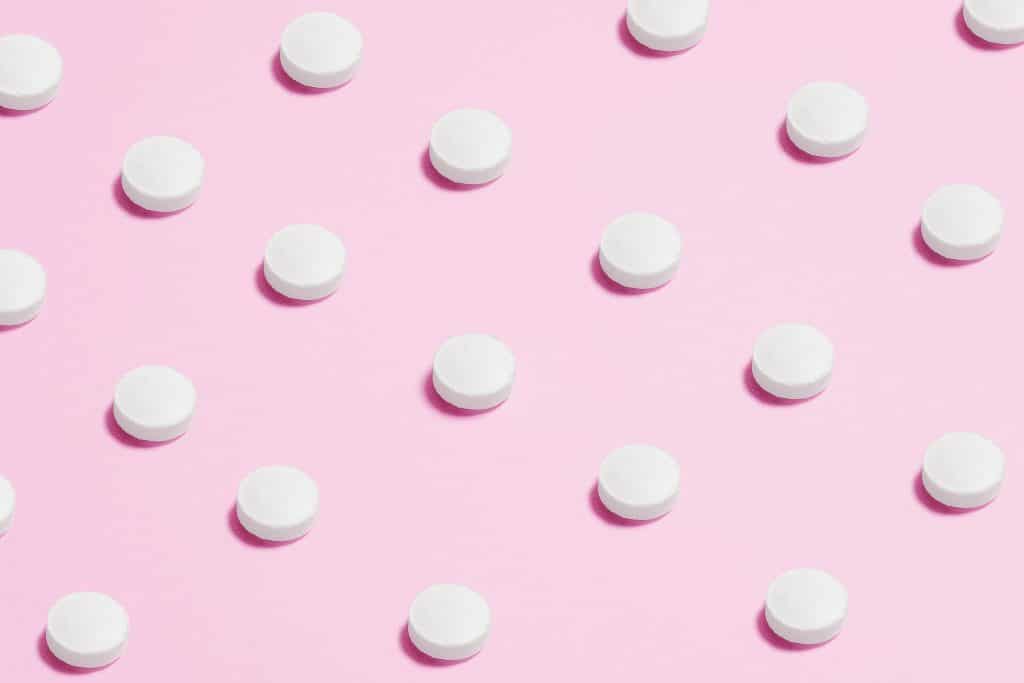 Flat lay of white pills on a pastel pink surface, showcasing a medical theme.