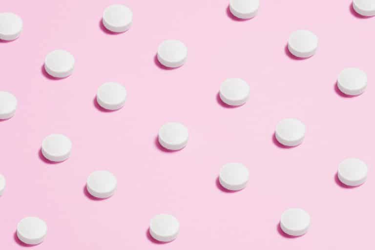 Flat lay of white pills on a pastel pink surface, showcasing a medical theme.