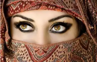 Woman with traditional patterned headscarf and striking eye makeup using eco-friendly kohl or kajal.